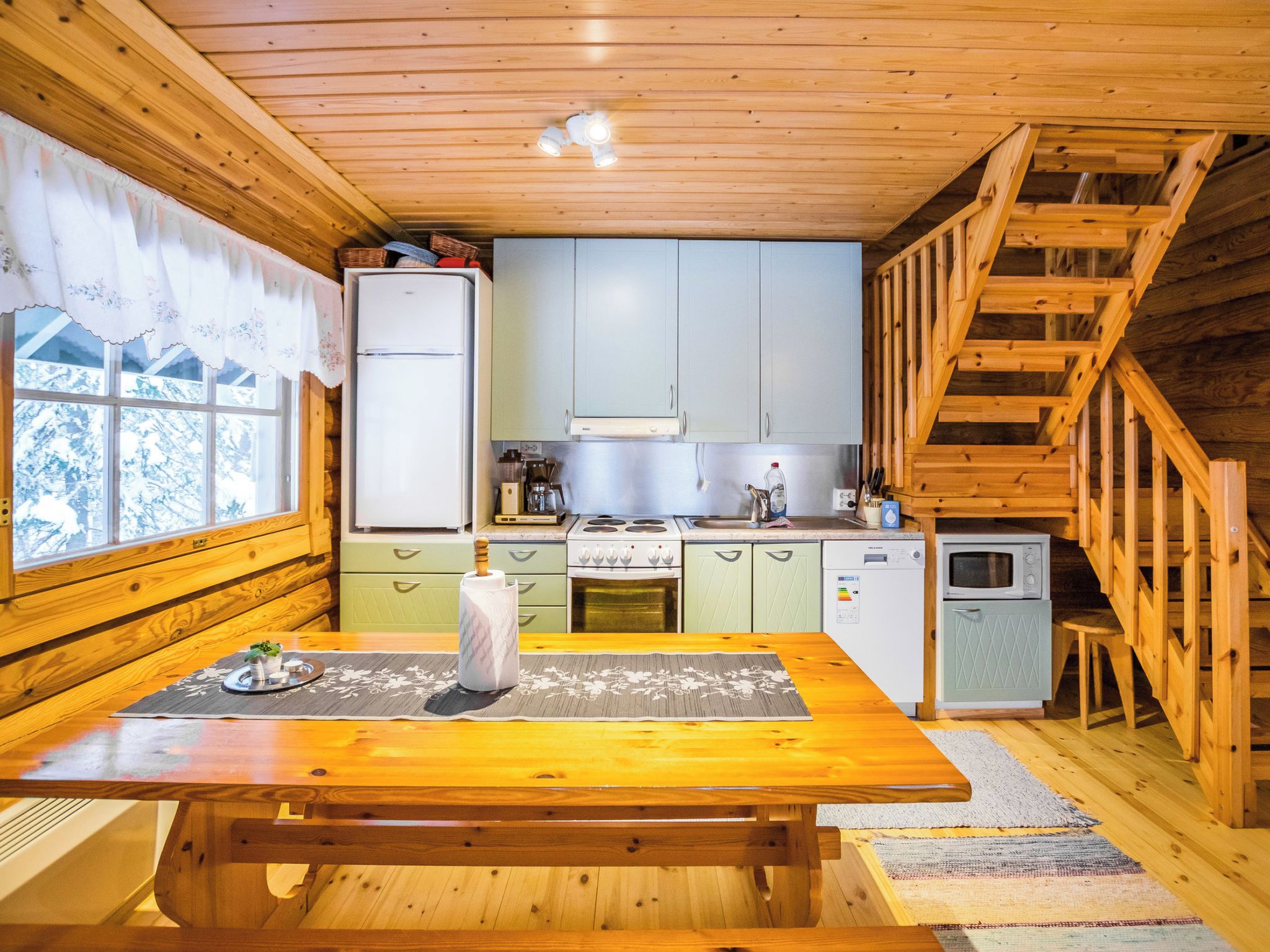 A cabin-style kitchen with wooden walls, a dining table, and a staircase.
