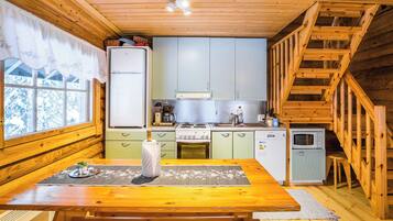 A cabin-style kitchen with wooden walls, a dining table, and a staircase.