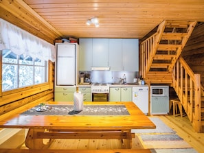 Et køkken i sommerhusstil med trævægge, et spisebord og en trappe.