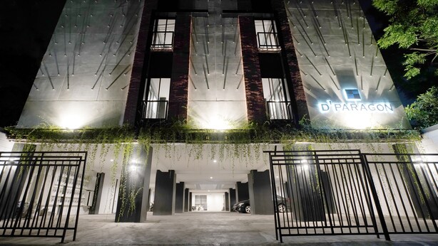 A modern building with a sign reading "D'PARAGON" at the entrance, featuring a gated driveway and hanging plants. - Dparagon Pogung F (Depok)