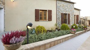 Un bâtiment doté d’une façade en pierre, de volets en bois et d’un jardin aménagé avec différentes espèces de plantes.