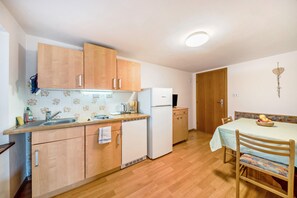 Una cocina compacta con armarios de madera, un refrigerador blanco y una zona de comedor con una mesa y sillas.