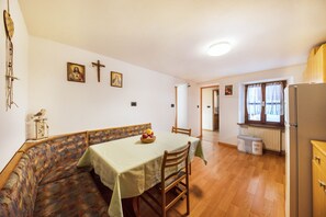 A dining area with a table, chairs, a bench, a fruit bowl, and a refrigerator.