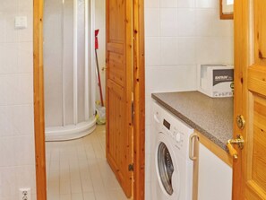 A laundry room with a washing machine, a countertop, and a door leading to a shower area.