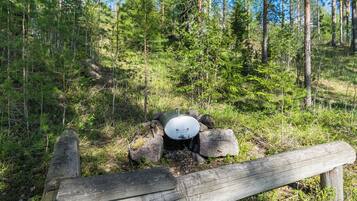 A forested area with a metal barrel and rocks, a wooden fence, and a clear sky.