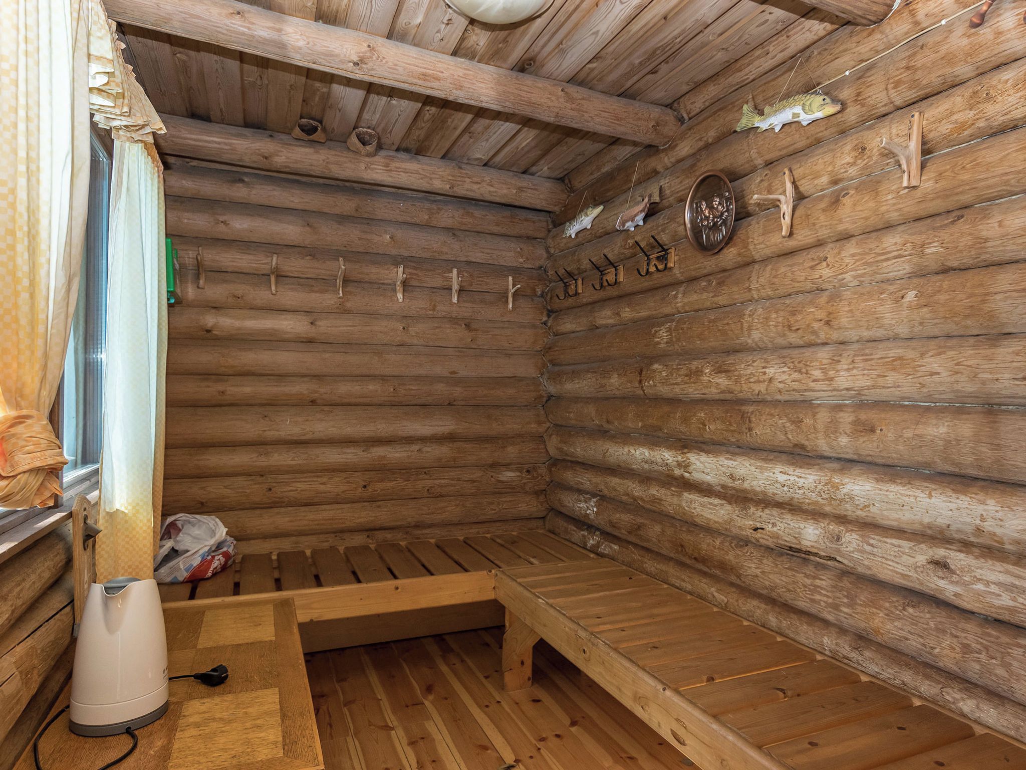 A wooden sauna room with benches, a heater, and decorative fish hooks on the wall.