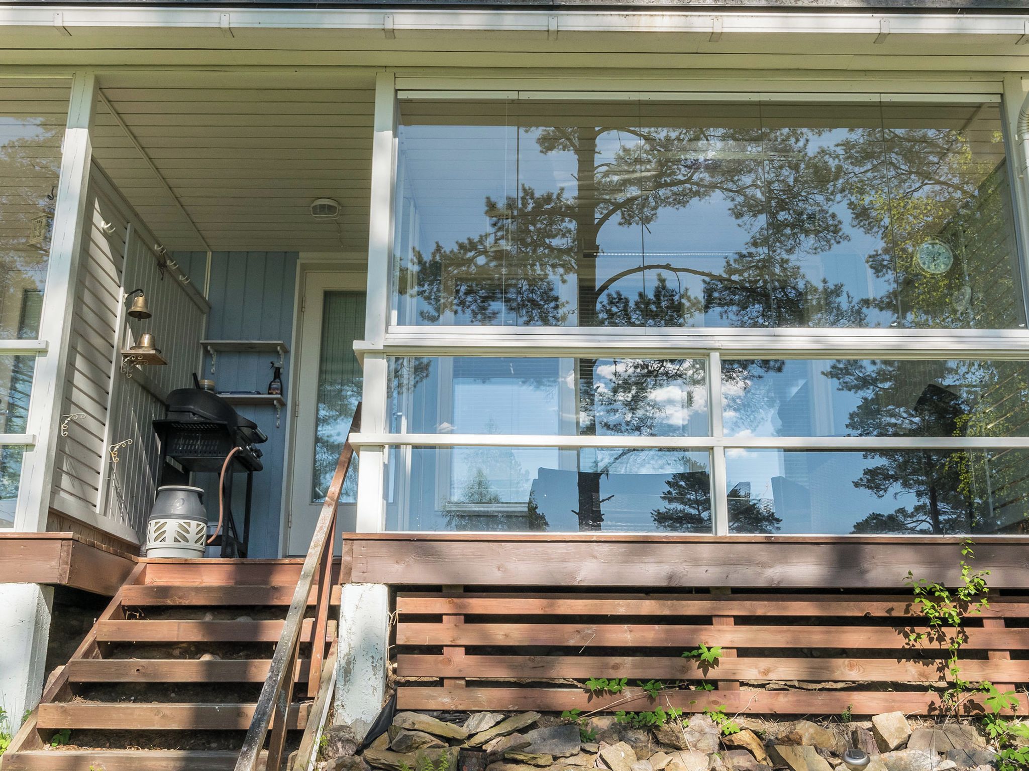 A wooden staircase leading to a porch with a large glass window reflecting trees.