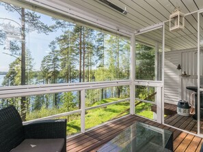 A covered outdoor area with a glass table and chairs, overlooking a lake and forest.