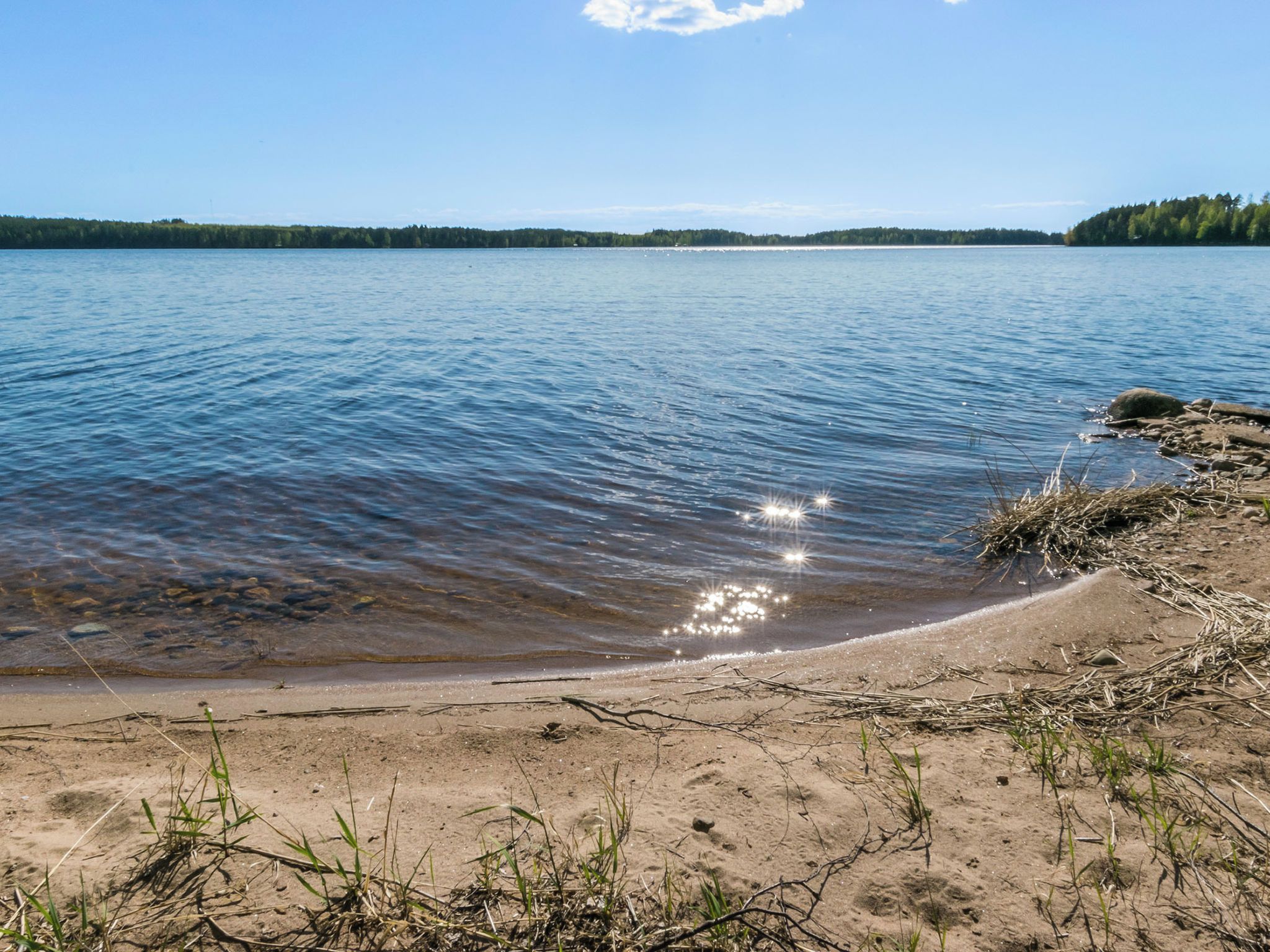 A clear lake with a sandy shore and a forested island in the distance.