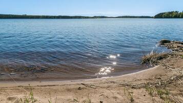 A clear lake with a sandy shore and a forested island in the distance.