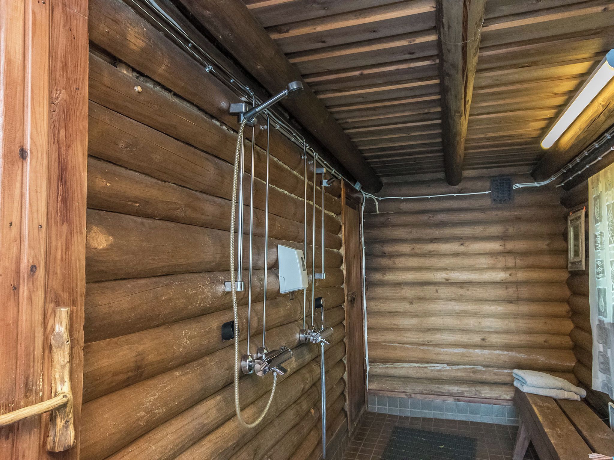 Interieur van een blokhut met een houten bank, een doucheruimte met metalen details en een betegelde vloer.