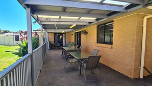 Un patio couvert avec une table et des chaises, un mur en briques et une vue sur le jardin.