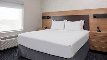 Ein Hotelzimmer mit einem großen Bett, einem Nachttisch, einem Heizkörper, einem Fenster und einer wandmontierten Bedieneinheit.