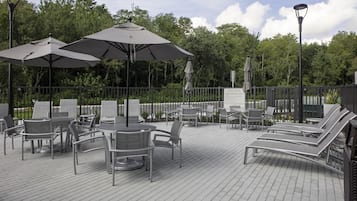 Ein möblierter Terrassenbereich mit Metalltischen, Stühlen, Sonnenschirmen und Liegestühlen.