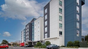 A multi-story hotel with a modern design, featuring a mix of white and dark blue exterior walls, large windows, and a parking area with several cars. - TownePlace Suites by Marriott Orlando Airport (Orlando)