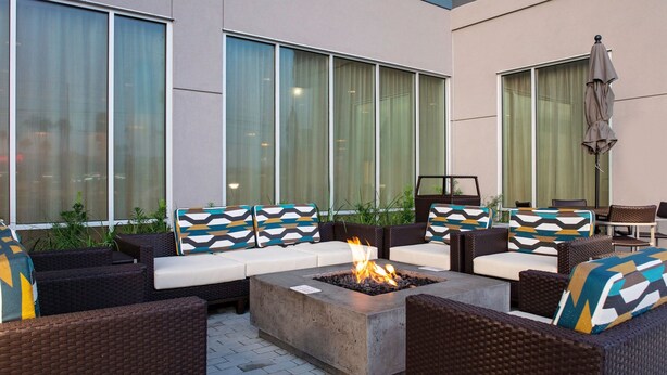 An outdoor seating area with wicker furniture, a central fire pit, and large windows. - TownePlace Suites by Marriott Orlando Airport (Orlando)