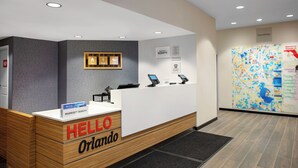 A hotel reception desk with a 'HELLO Orlando' sign, a digital screen, and a map on the wall. - TownePlace Suites by Marriott Orlando Airport (Orlando)