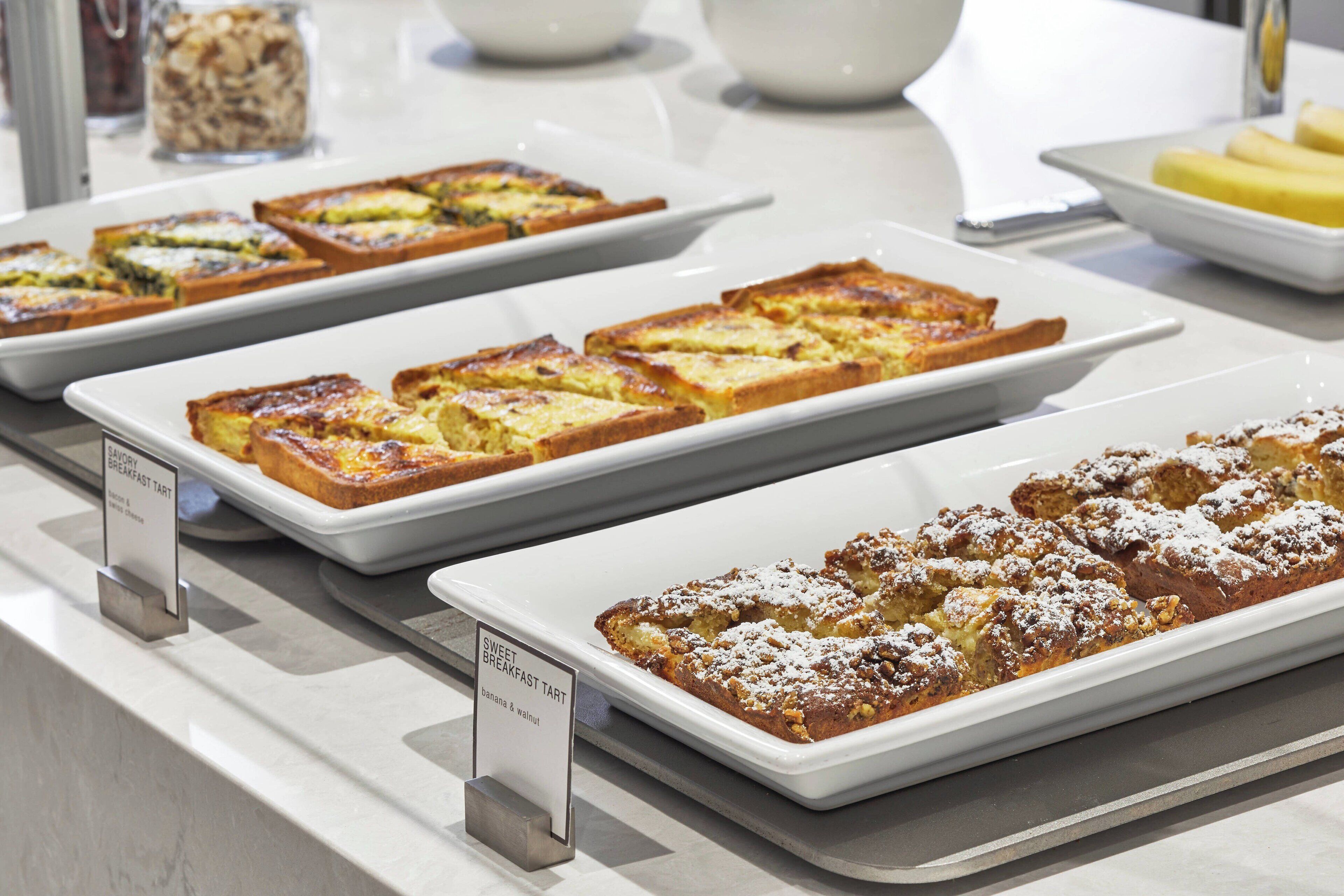 A breakfast buffet with various pastries and a sign indicating a sweet breakfast tart with banana and walnut.