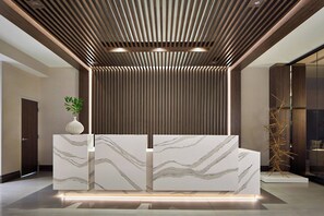 A reception area with a modern design, featuring a marble reception desk, a wooden slatted ceiling, and a minimalist decor.