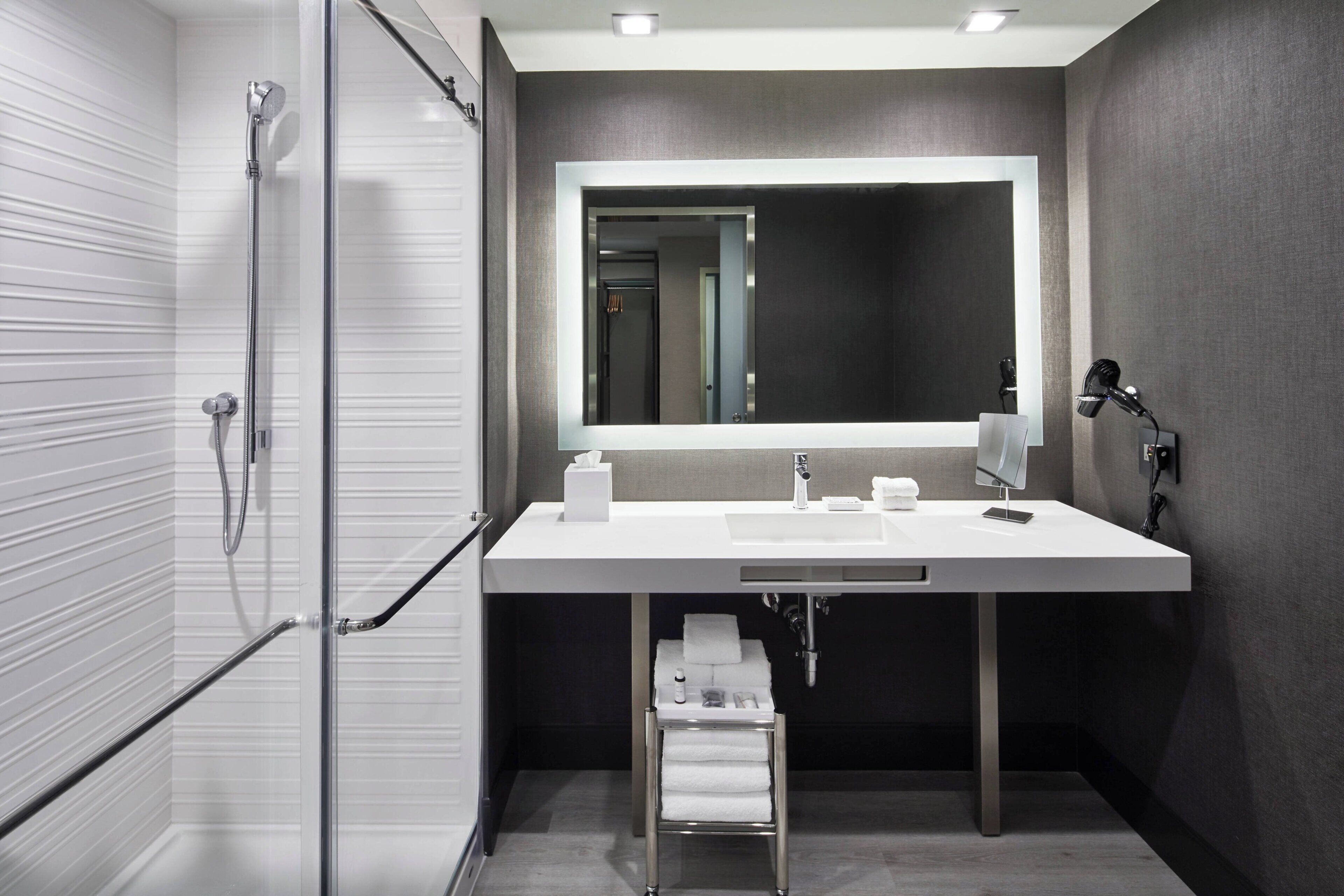 A modern bathroom with a glass shower enclosure, a white sink with a large mirror, and a towel rack.