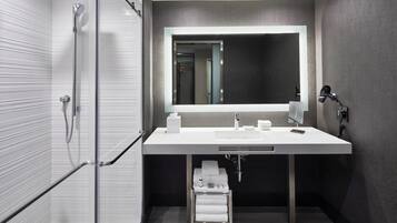 A modern bathroom with a glass shower enclosure, a white sink with a large mirror, and a towel rack.