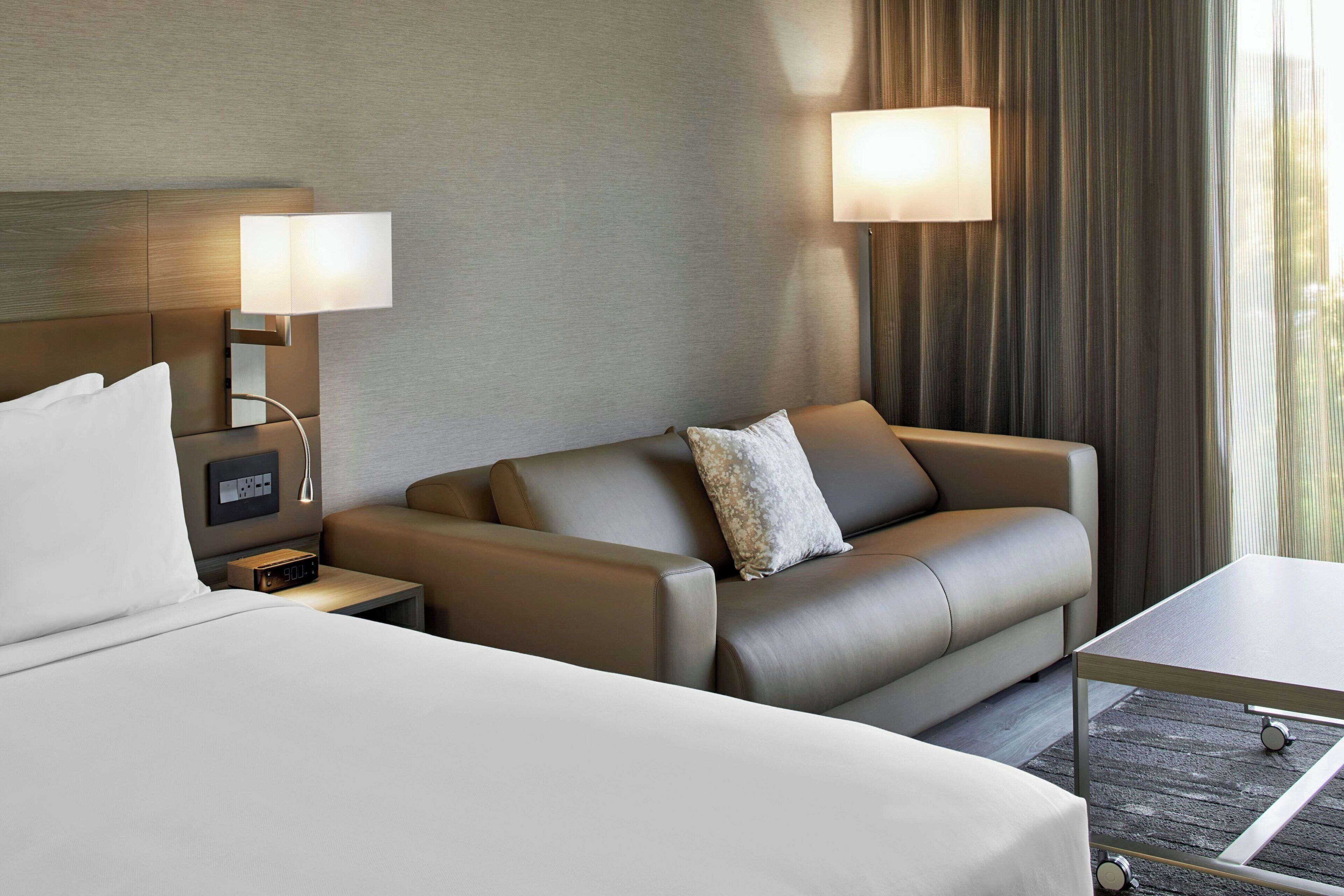 Una habitación de hotel con una cama, un sofá, una mesa y dos lámparas fijadas a la pared.