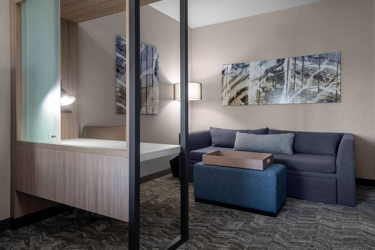 A modern hotel room with a bed, a sofa, a small table, and abstract art on the wall.