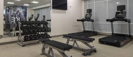 A gym with treadmills, a bench press, and a rack of dumbbells.