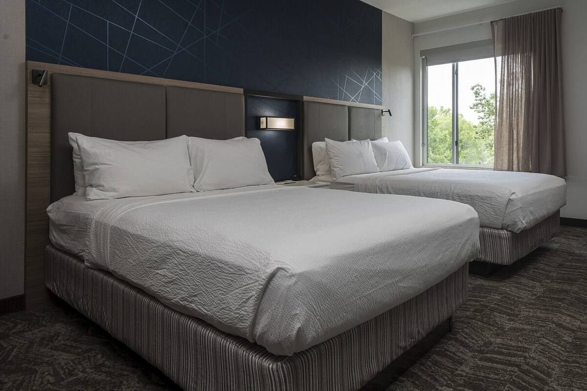 A hotel room with two beds, a large window with curtains, and a geometric wall design.
