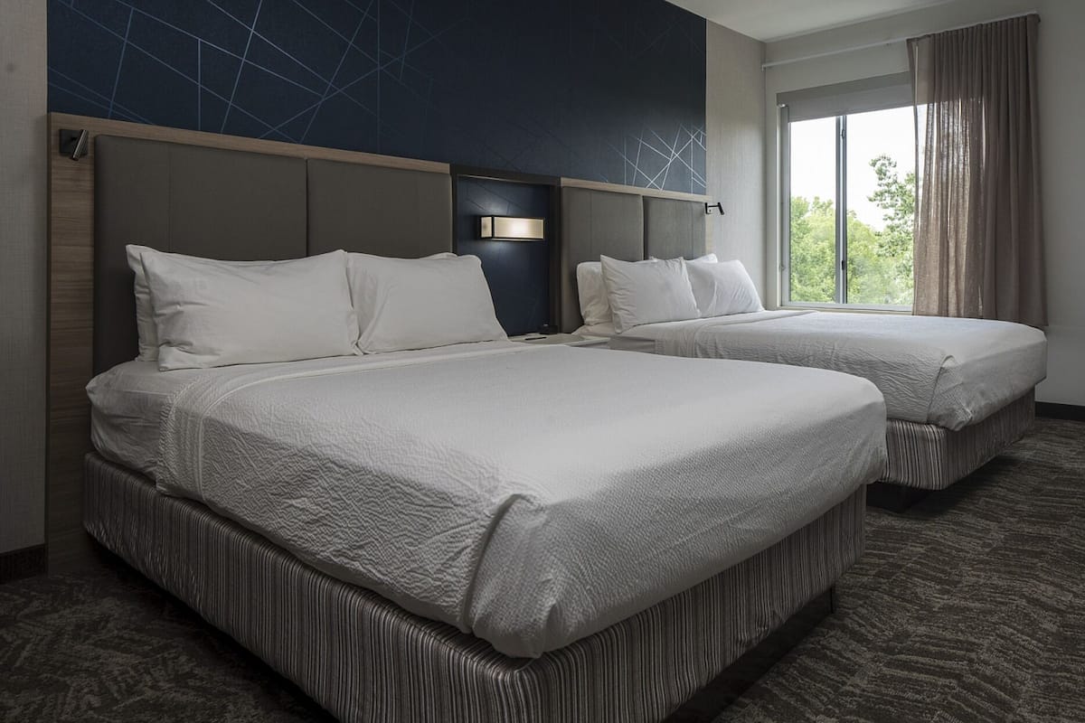 A hotel room with two beds, a large window with curtains, and a geometric wall design.
