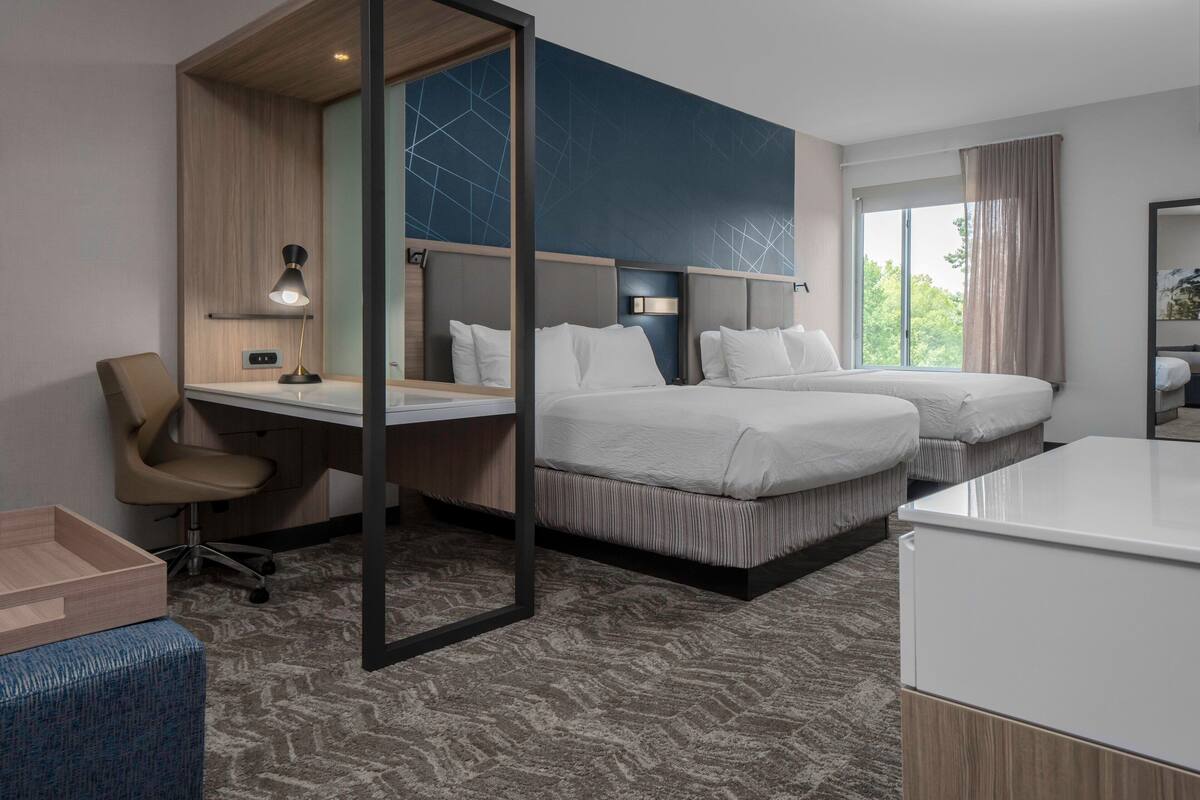 A hotel room with two beds, a desk, a chair, and a large window.