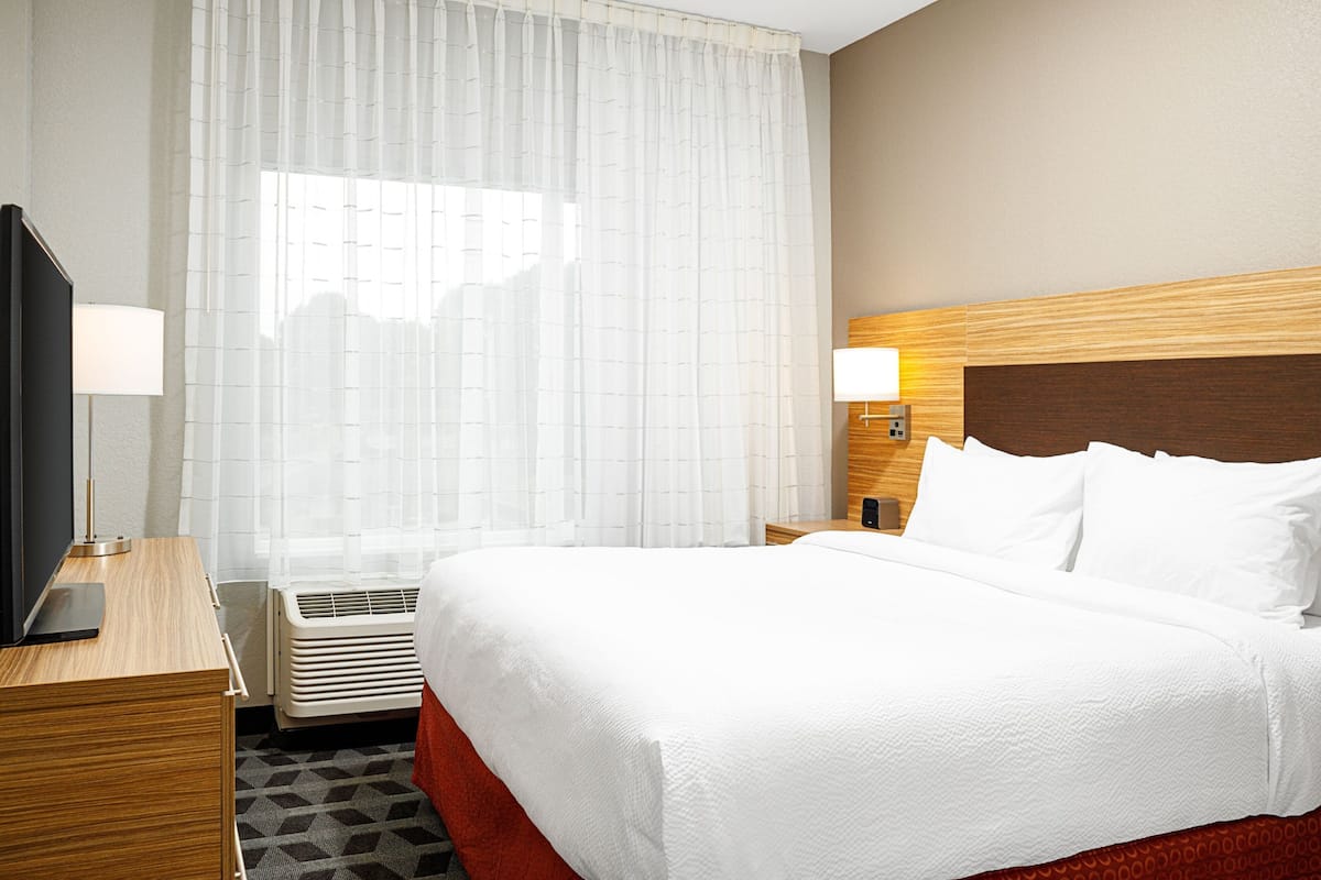 A hotel room with a bed, a desk with a lamp, a TV, and a window with curtains.