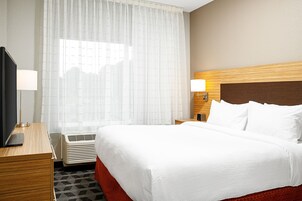 A hotel room with a bed, a desk with a lamp, a TV, and a window with curtains.
