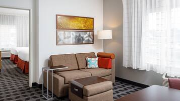 A hotel room with a sofa, a small table, a lamp, and a view of the outside through the window.