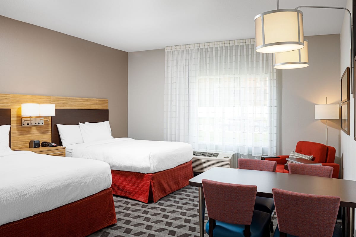 A hotel room with two beds, a desk, and a chair.