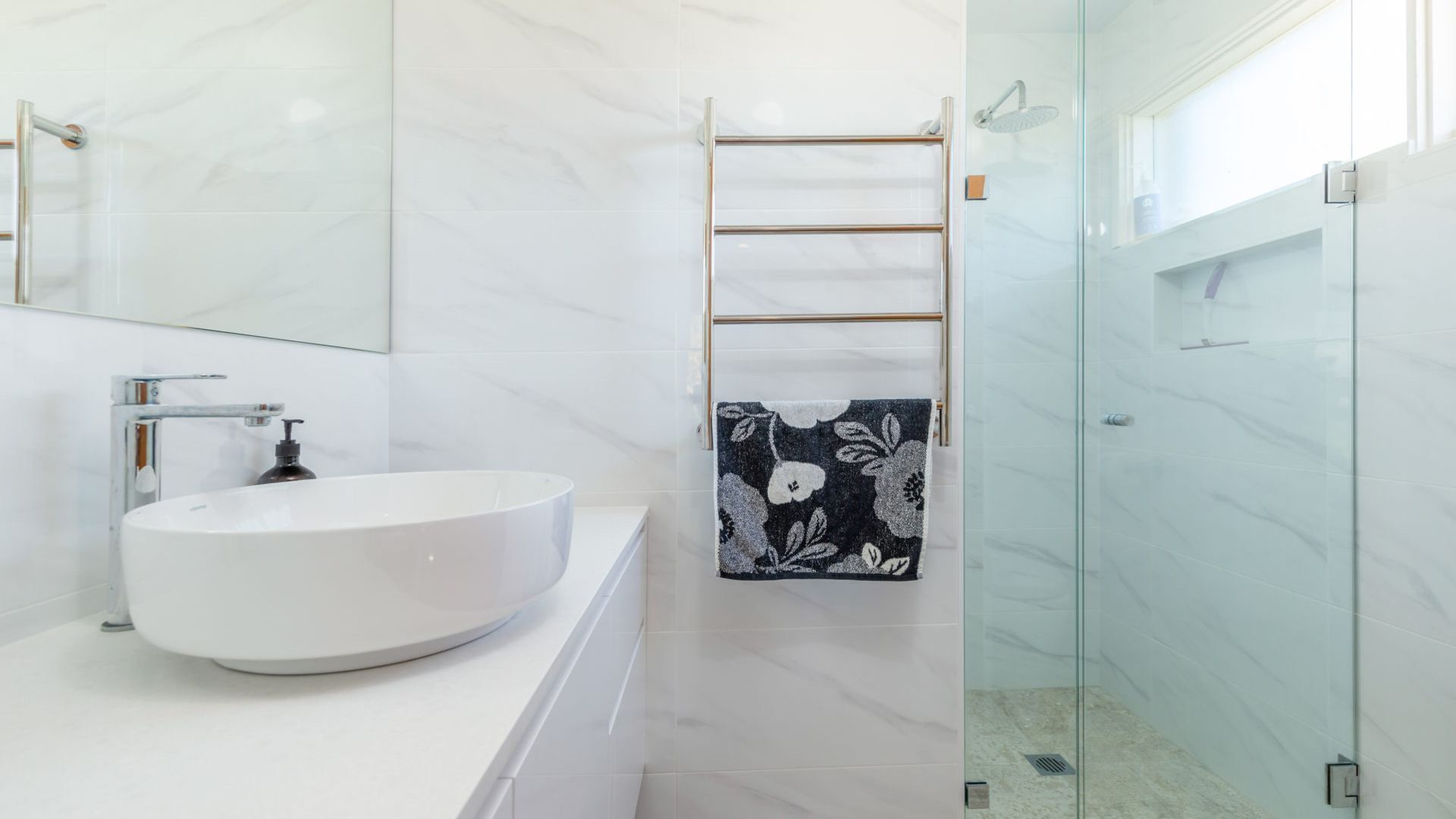 A modern bathroom with a white sink, a glass shower enclosure, and a towel rack with a floral towel.