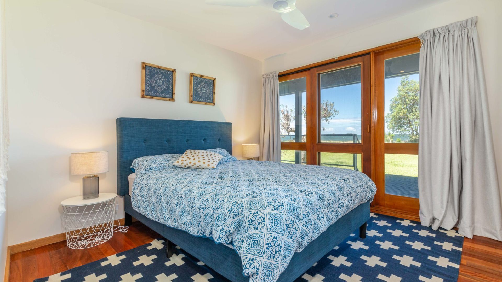 A bedroom with a large bed, two bedside lamps, a wooden headboard, and a view of the outdoors through a sliding glass door.
