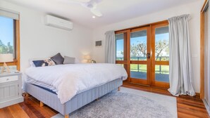 Een slaapkamer met een groot bed, een nachtkastje, een lamp en uitzicht op de natuur via een schuifdeur.
