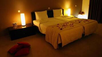 Quarto de hotel com duas camas, uma mesa de cabeceira e uma cadeira vermelha.