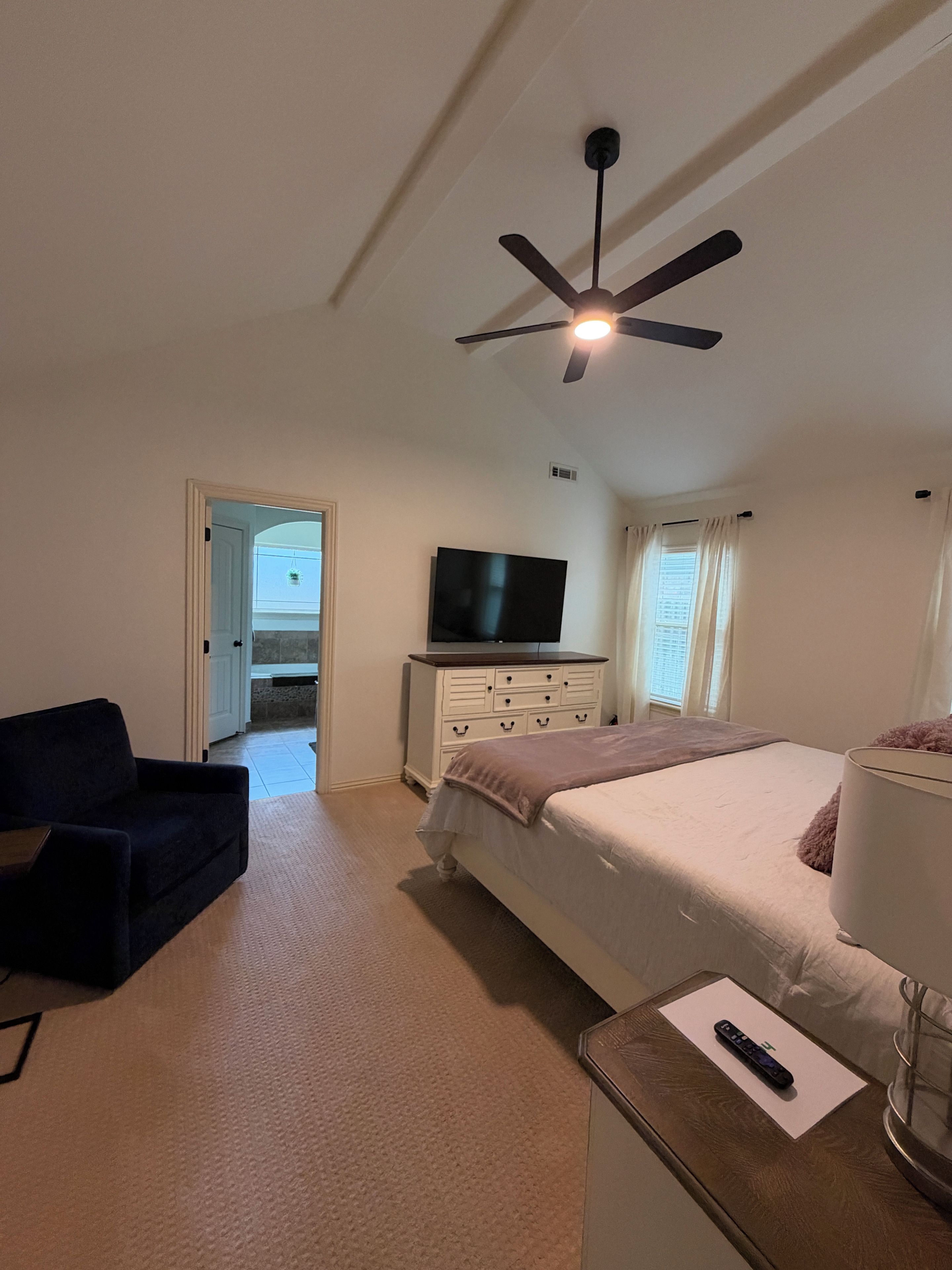 A hotel room with a bed, a TV, a ceiling fan, a desk, and a chair.