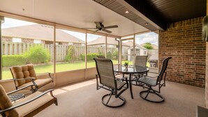 A covered patio with a glass table and chairs, a ceiling fan, and a view of a backyard with a wooden fence. - Bikers Paradise , Trails, Promenade Mall, AMP, Restaurants, and Top Golf (Rogers)