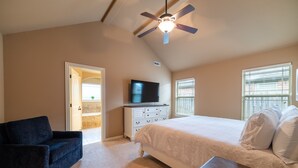 A bedroom with a bed, a ceiling fan, a TV, a dresser, and a door leading to another room. - Bikers Paradise , Trails, Promenade Mall, AMP, Restaurants, and Top Golf (Rogers)