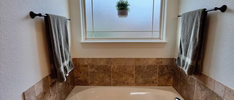 A bathroom with a bathtub, a window with a hanging plant, and towels on towel racks.