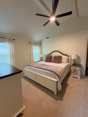 A bedroom with a bed, bedside tables, a ceiling fan, and a window with curtains.