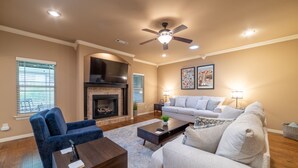A living room with a fireplace, a ceiling fan, and a large window with blinds. - Bikers Paradise , Trails, Promenade Mall, AMP, Restaurants, and Top Golf (Rogers)
