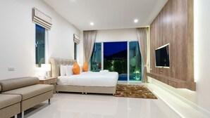 Een moderne slaapkamer met een groot bed, een bank, een televisie en uitzicht op een zwembad 's nachts.
