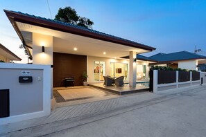 Une maison moderne dotée d’un porche abrité, d’un espace salon extérieur et d’une piscine visible.