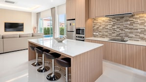 Een moderne keuken met een centraal eiland, barstoelen, geïntegreerde apparatuur en uitzicht op de omgeving.