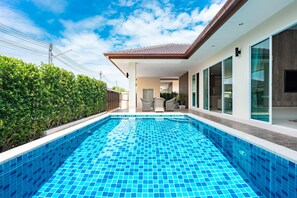 Une maison moderne dotée d’une piscine, de grandes fenêtres et d’un patio couvert.