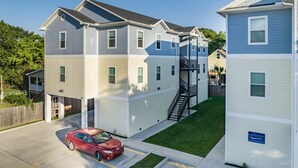 Un edificio residencial de varios pisos con una escalera central, un automóvil estacionado en la entrada y un césped bien cuidado.